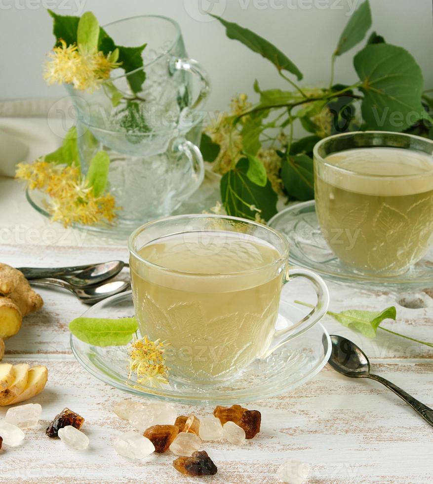 taza transparente con té de jengibre y tilo en una tabla de madera blanca foto