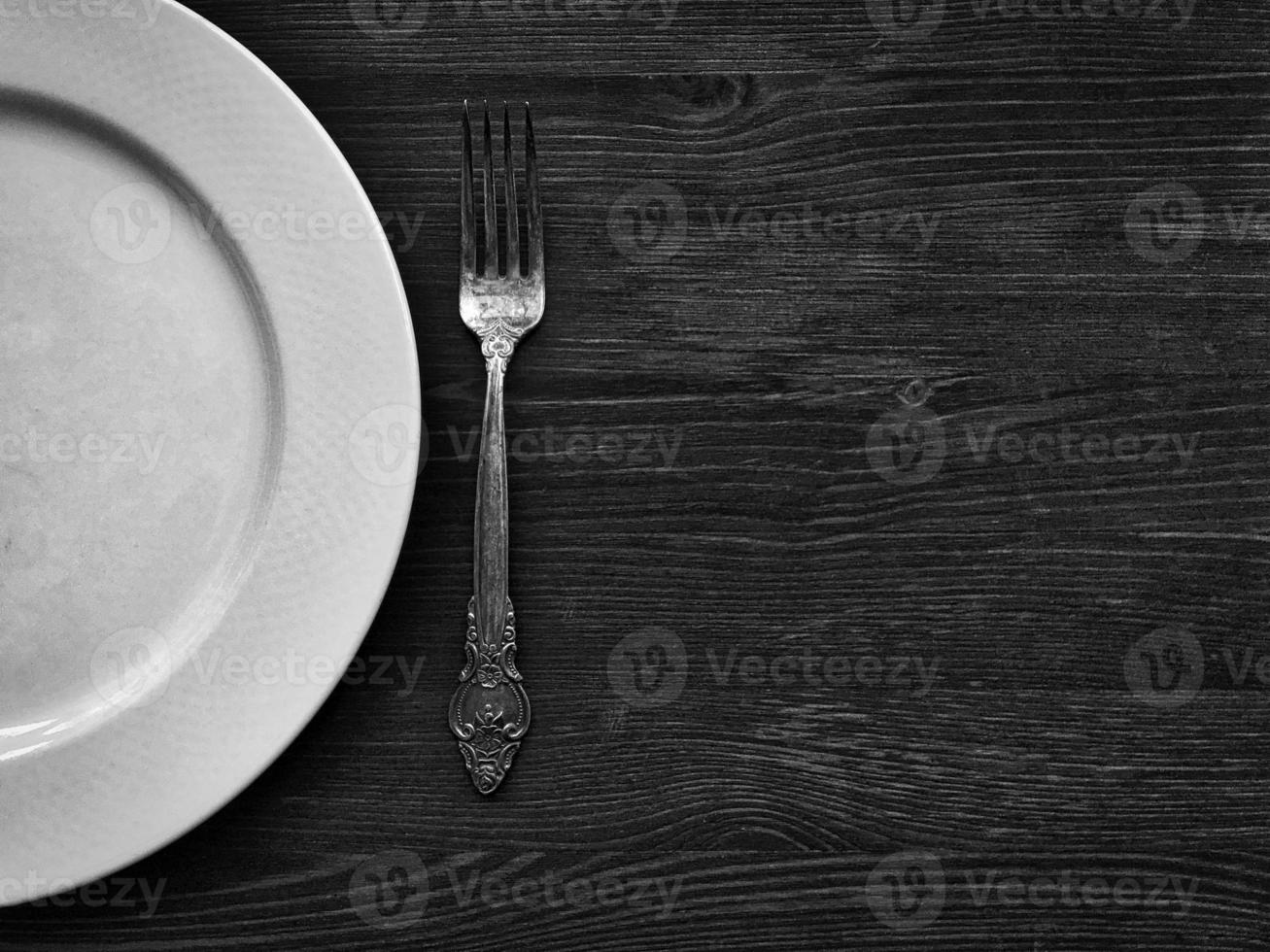 Empty white plate with a fork on a wooden surface, black and white photo