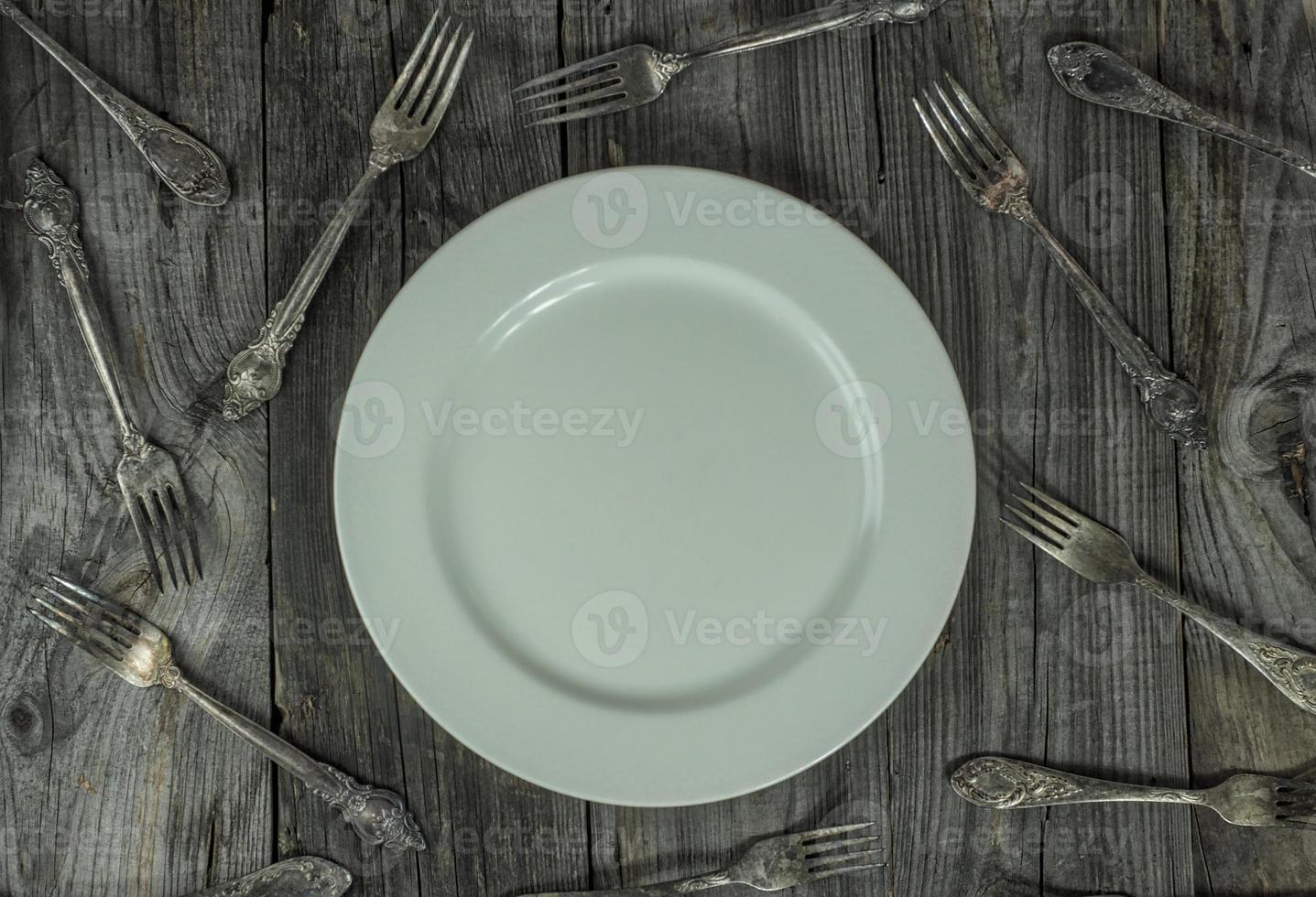 plato vacío sobre una superficie de madera gris, alrededor de muchos tenedores de hierro foto