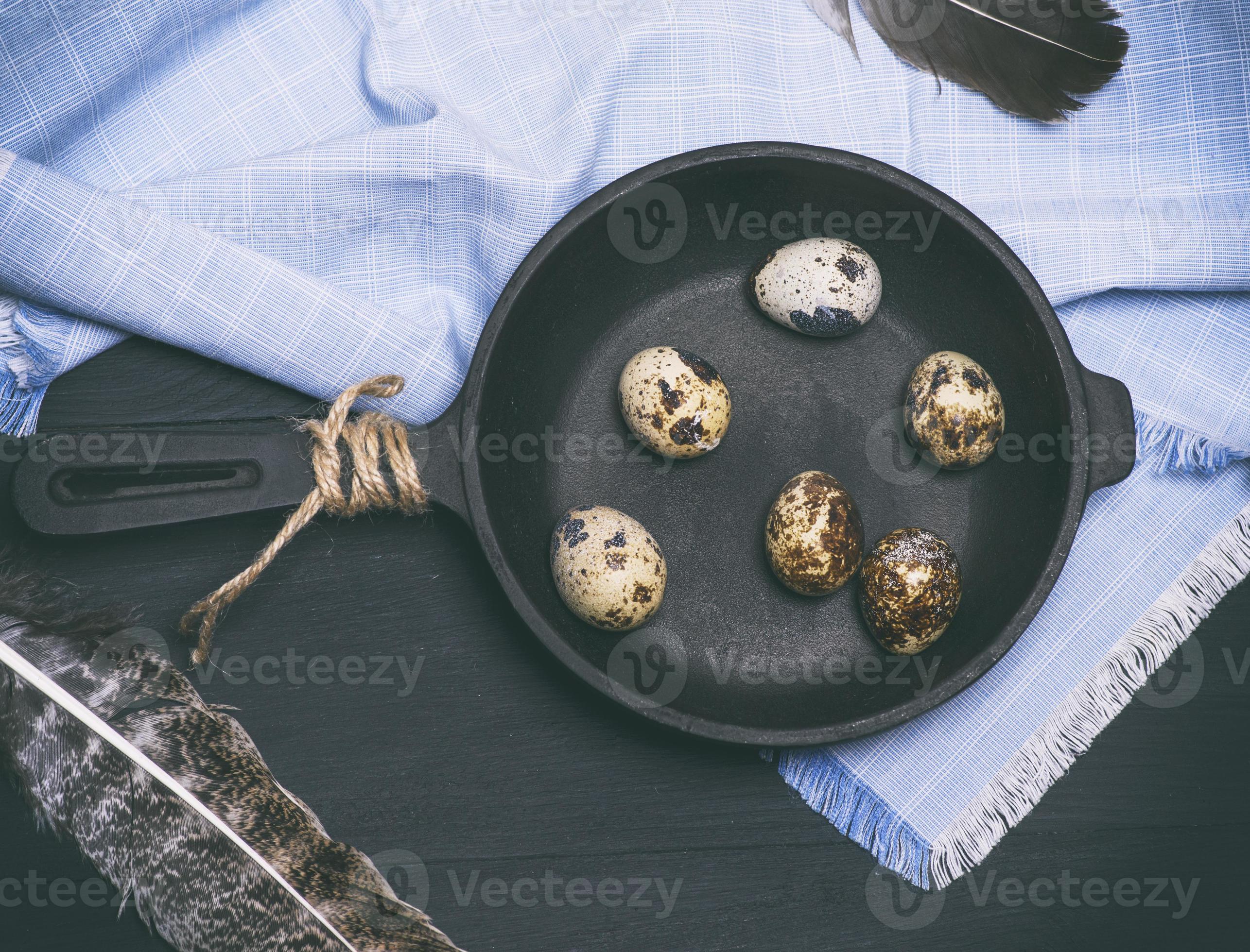 raw quail eggs in the shell lie in a black castiron frying pan