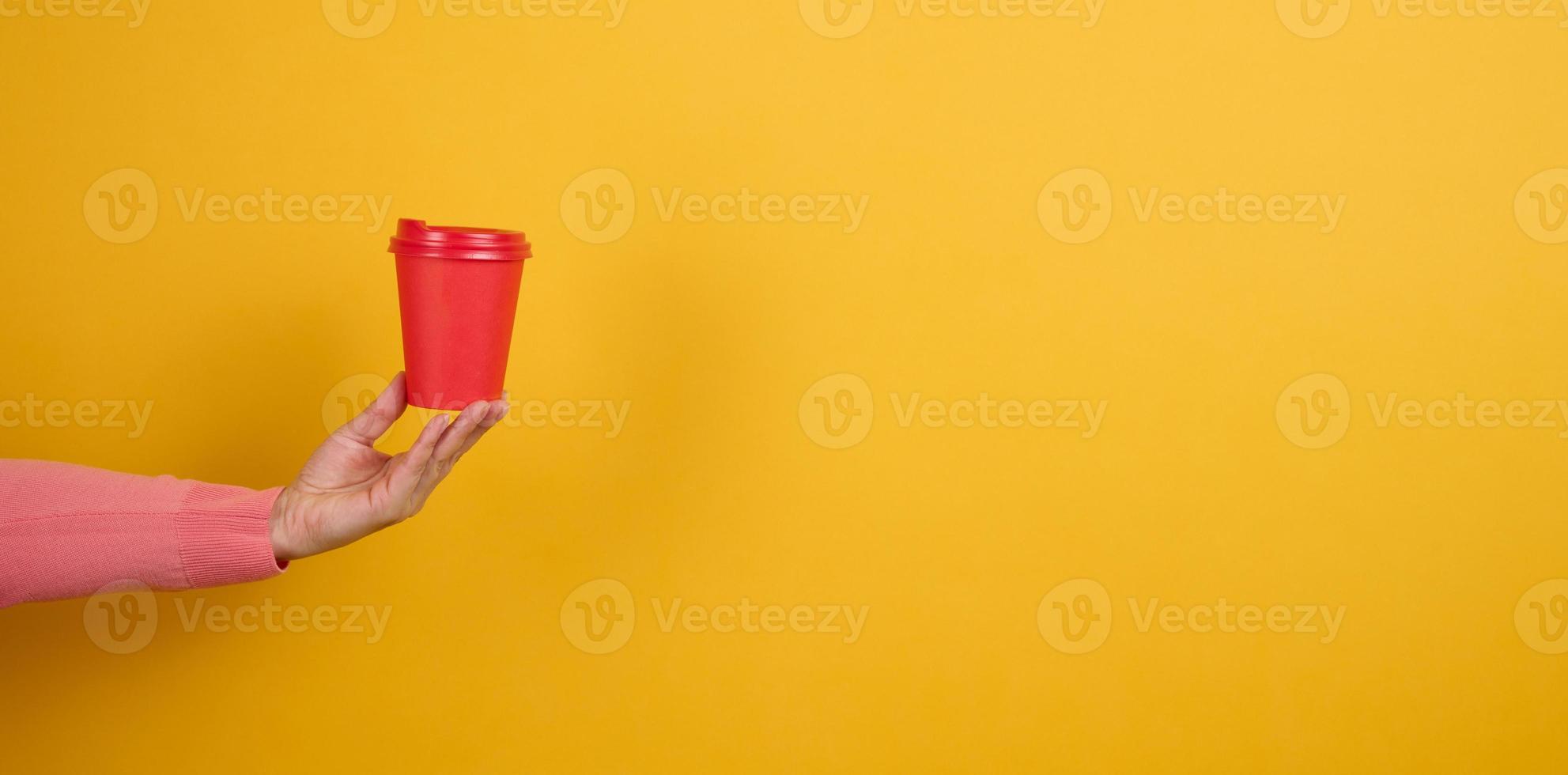hand holds paper cardboard red cup for coffee, yellow background. Eco-friendly tableware, copy space photo