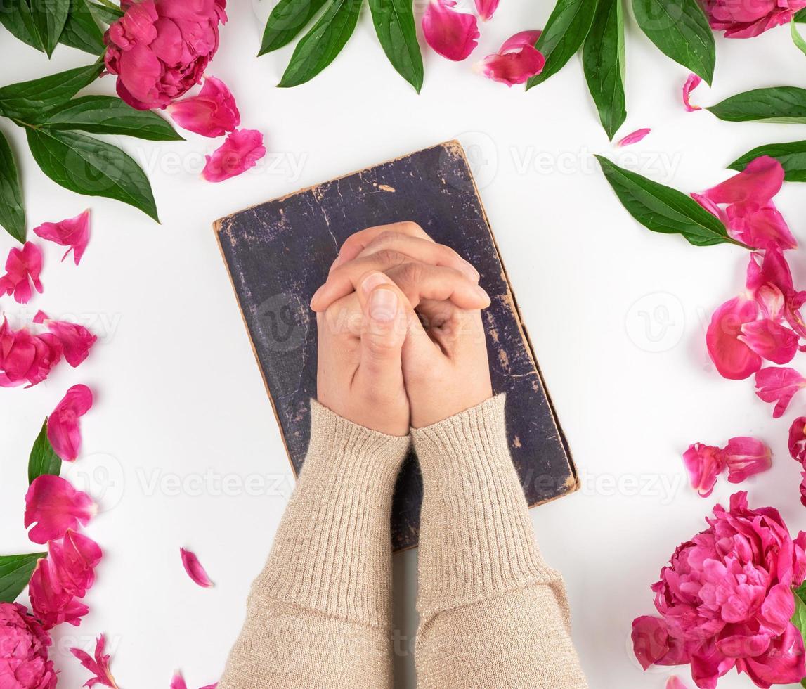 two hands lie on the old book in a gesture of prayer photo