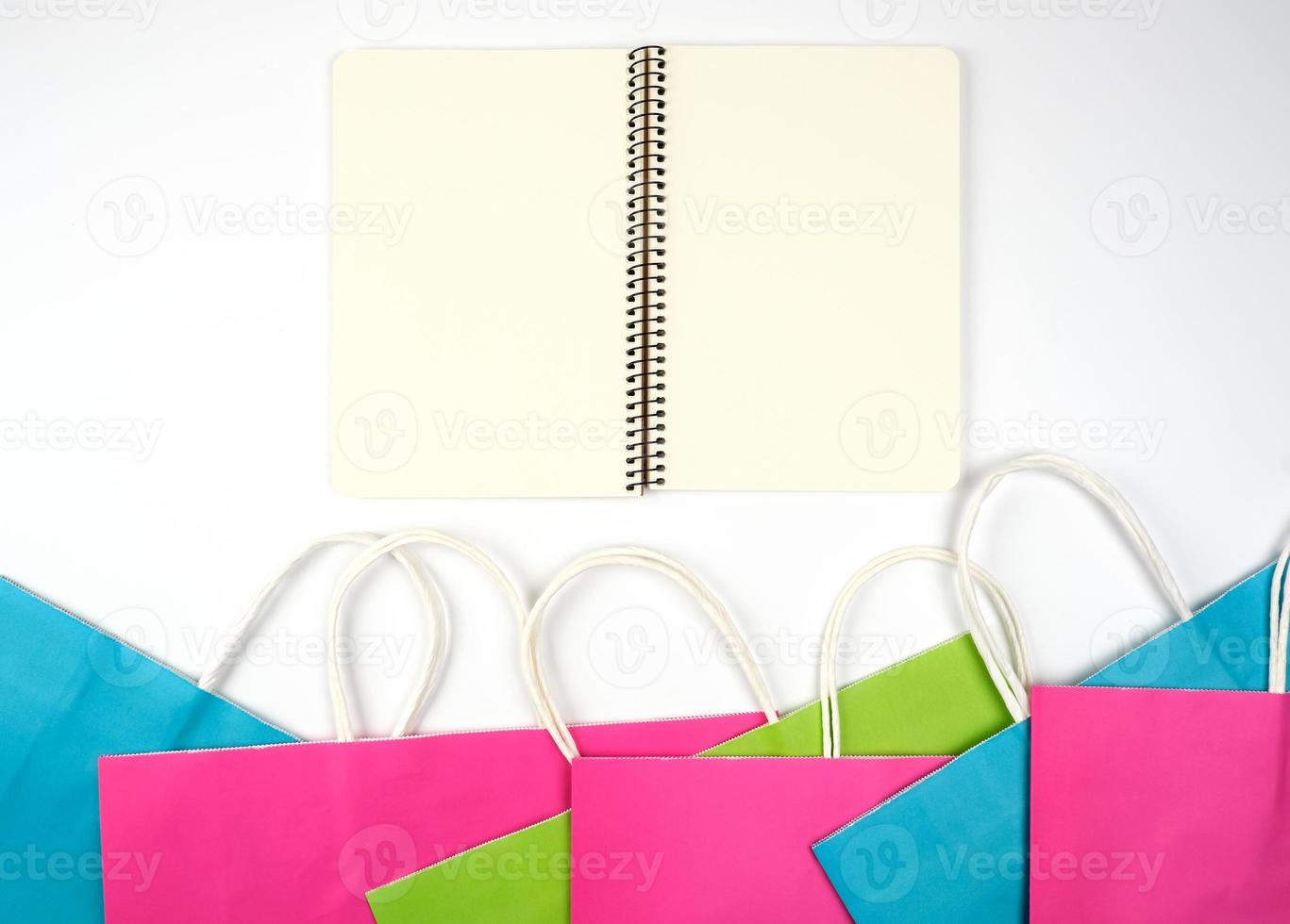 open notebook with blank white sheets and multi-colored paper shopping bags with white handles photo