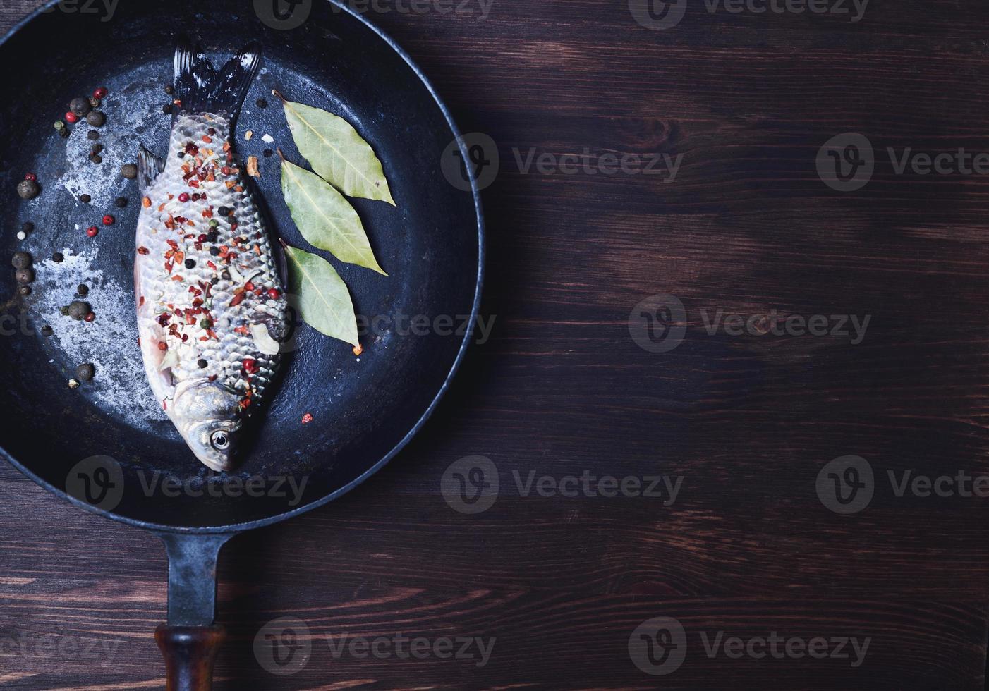 pescado de carpa con especias en una sartén de hierro fundido negro foto