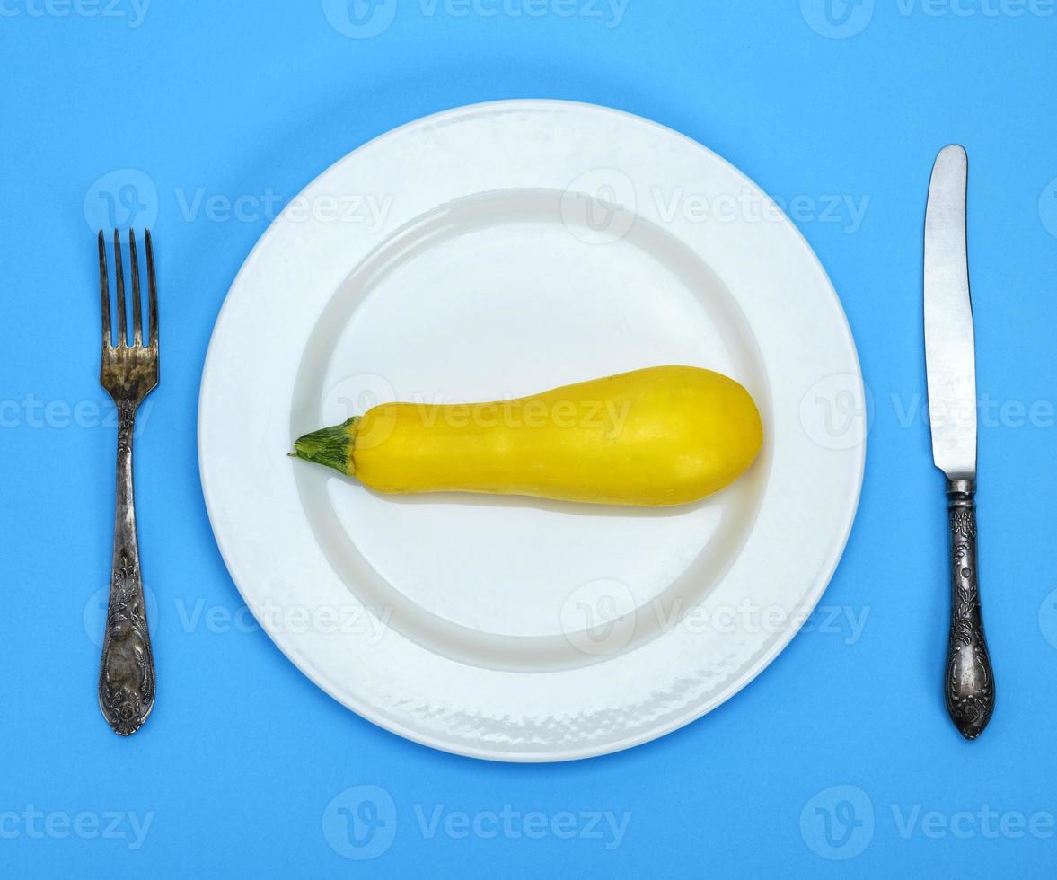 raw yellow squash in a white ceramic plate and iron fork with a knife photo