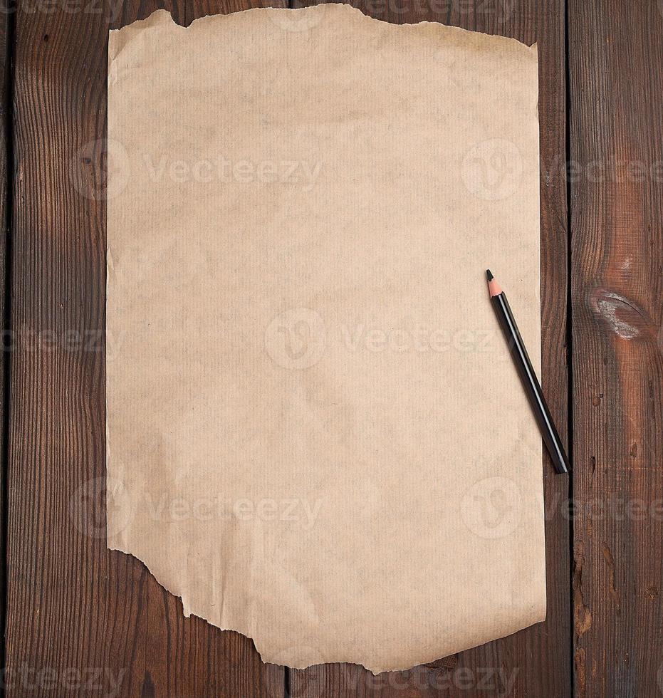 torn empty sheet of brown paper and a black pencil on a wooden surface photo