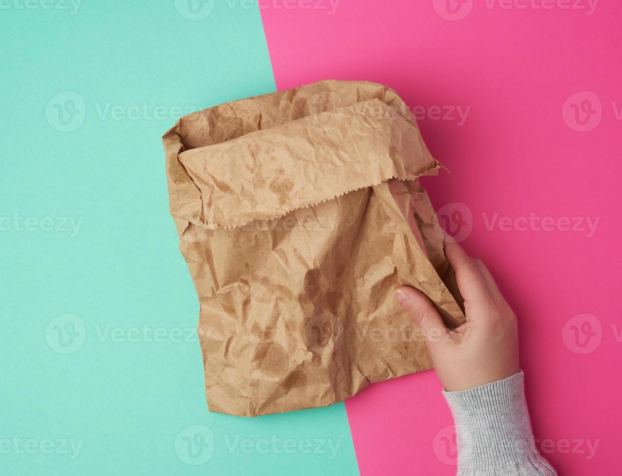two female hand holding open brown paper bag for food packaging with greasy stains on a green pink background photo