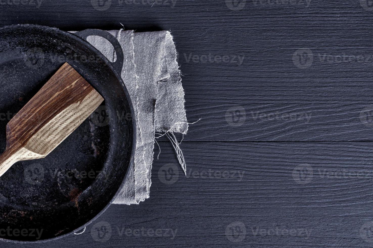 Frying pan with wooden spatula on a black surface photo