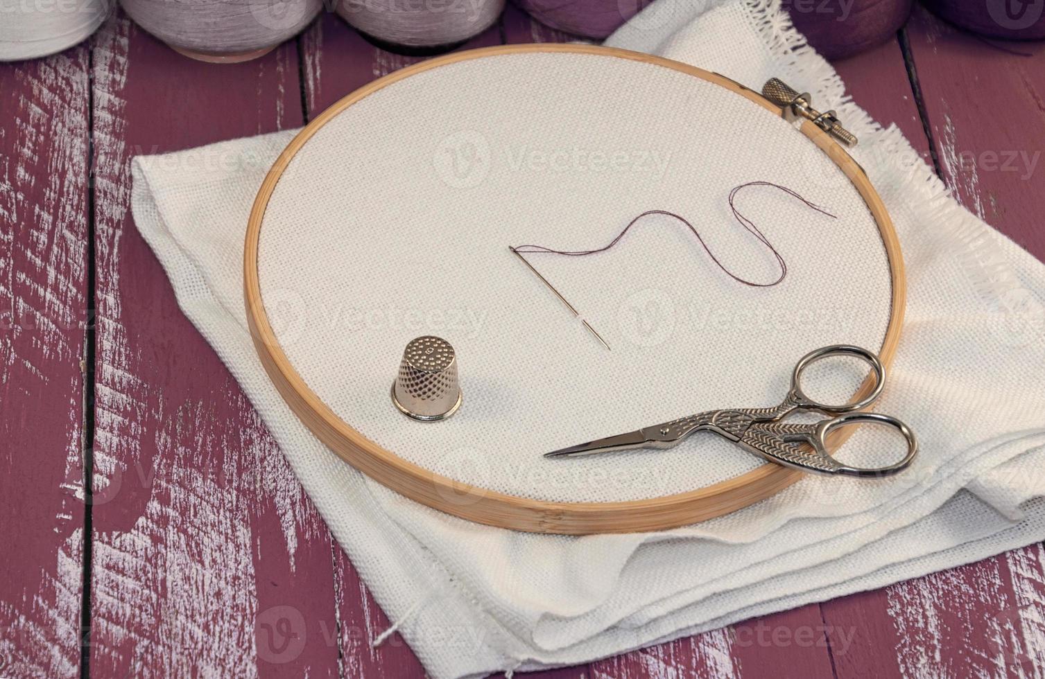 White fabric in the wooden embroidery frame with a set of threads in coils for needlework photo