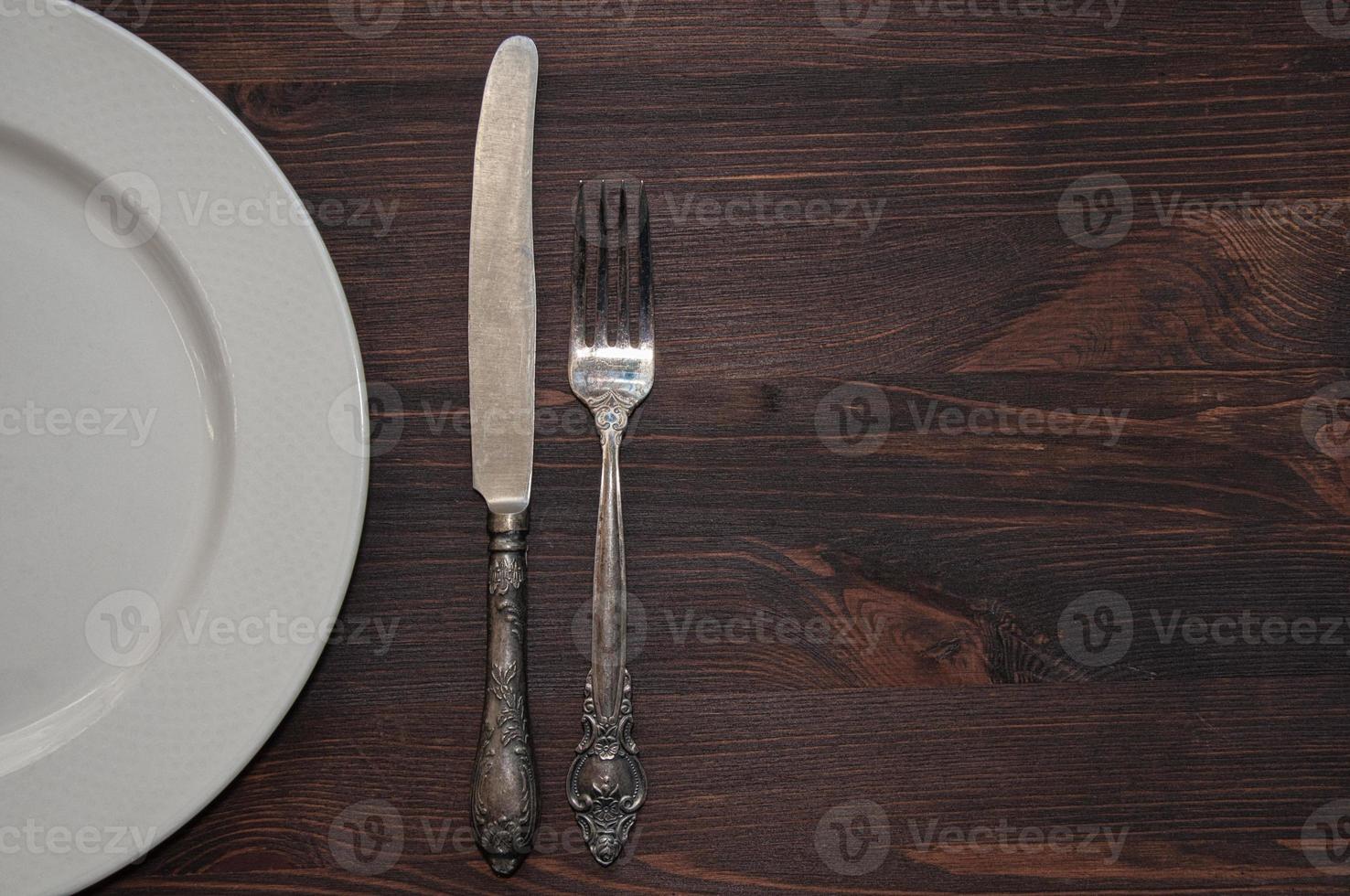 Half of an empty white plate with a fork and a knife on a brown table photo