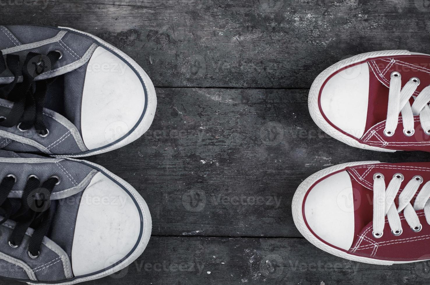 Two pairs of well-worn sneakers on a wooden surface photo