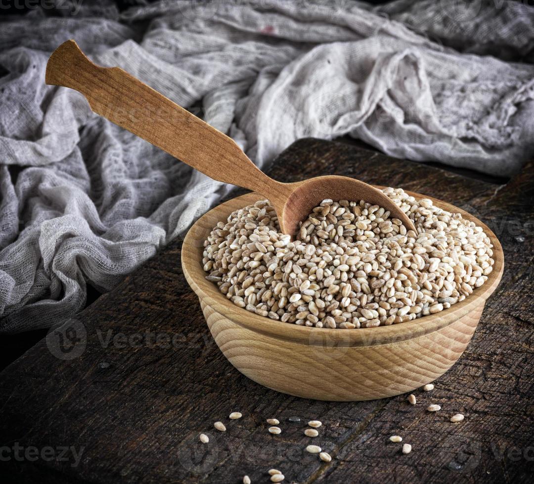 grano de trigo en un cuenco de madera sobre una mesa marrón foto