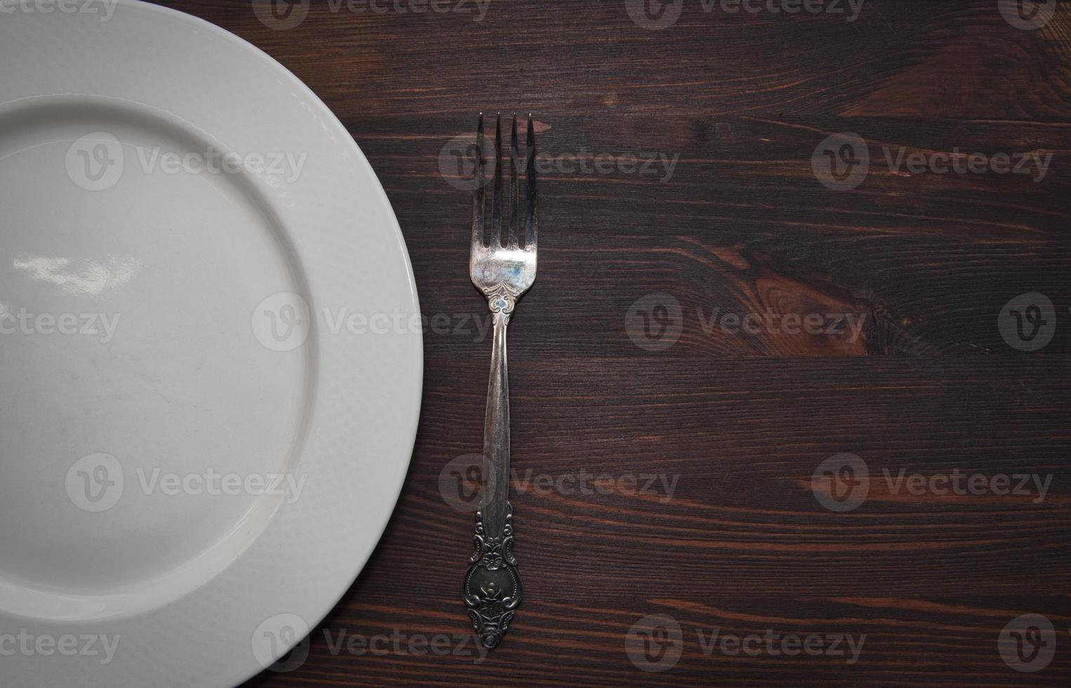 Empty white plate with a fork on a wooden brown surface photo