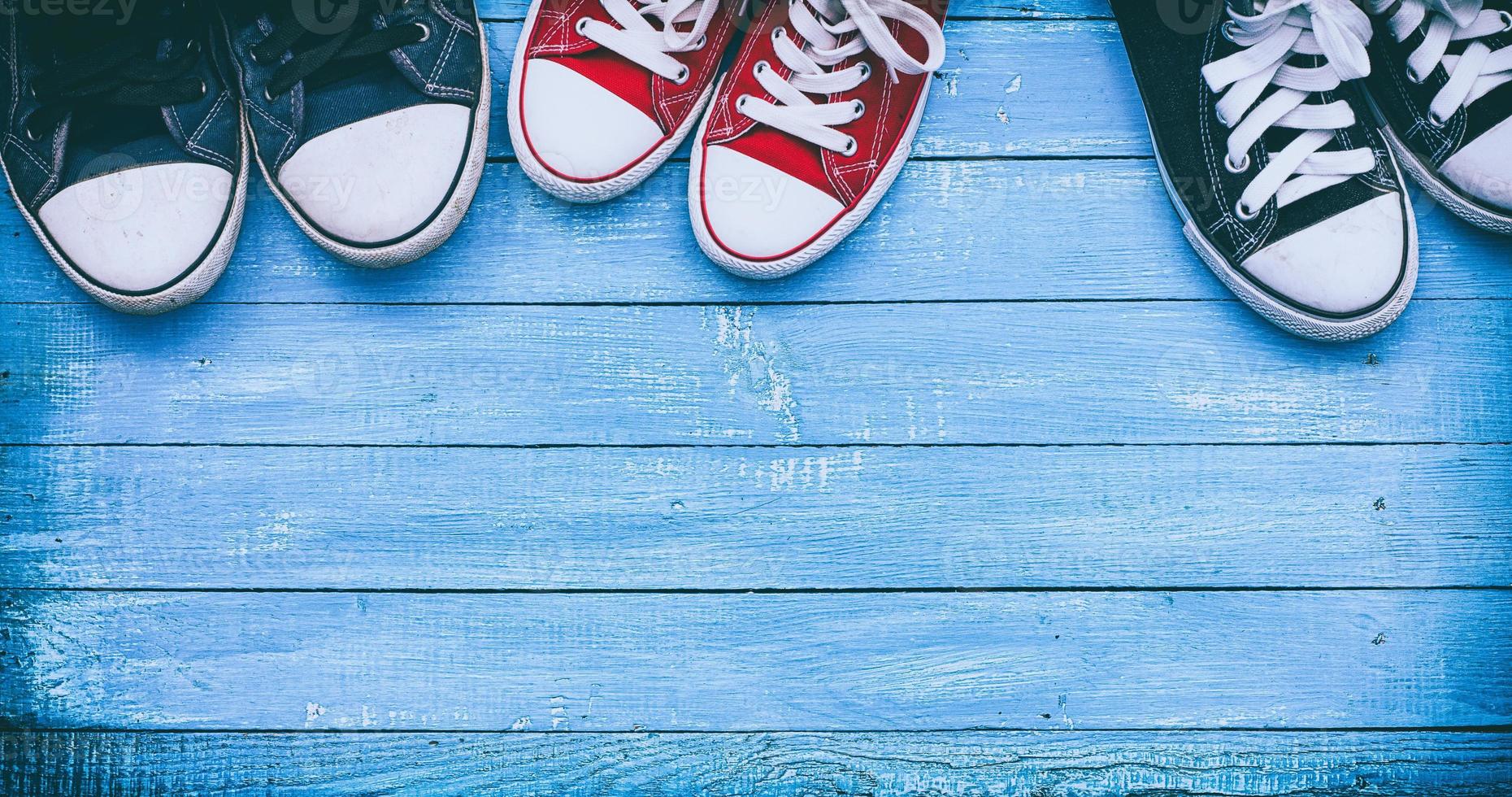 Three pairs of wearing sneakers on a blue wooden surface, top view photo