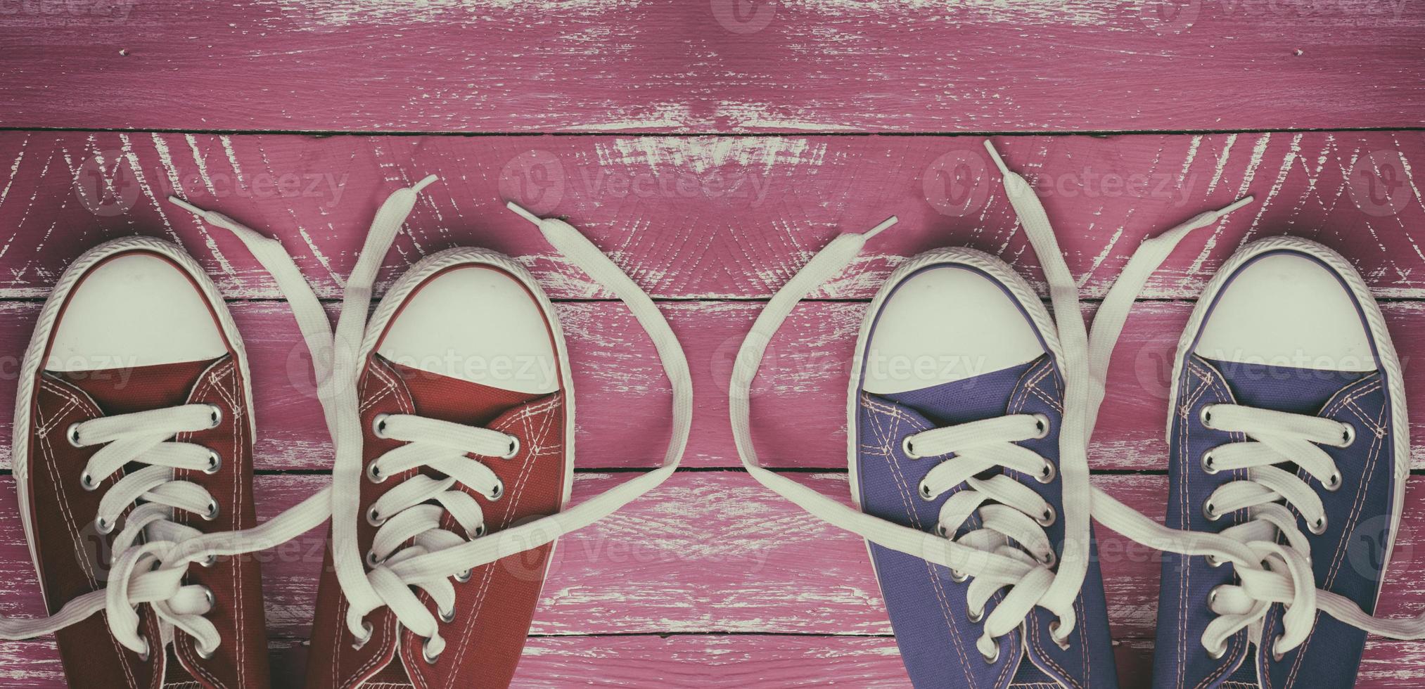 Two pairs of worn sneakers on a pink old wooden surface photo
