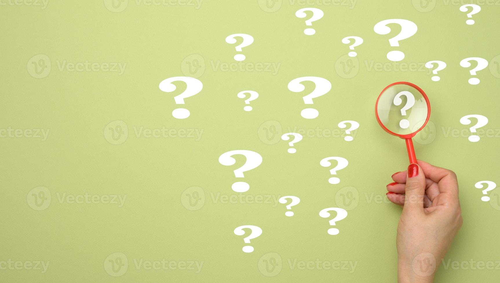 female hand holds a plastic magnifying glass and question marks on a green background. The concept of finding an answer to questions photo