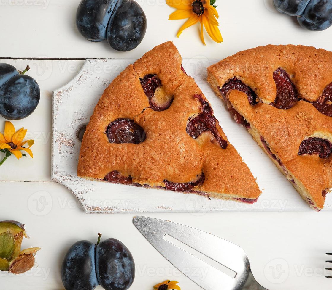 slices of biscuit plum cake on a white wooden board and fresh fruits photo