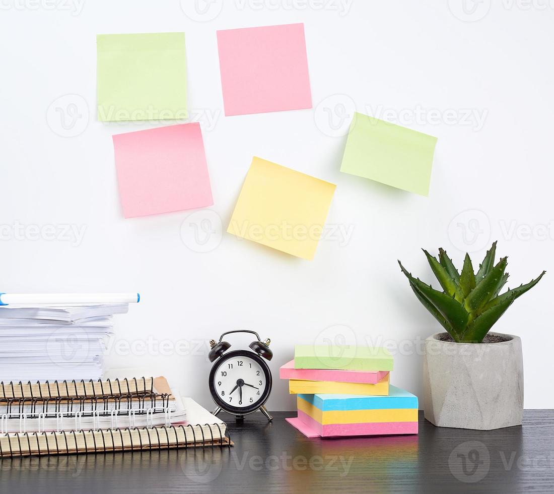 stack of spiral notebooks and colored stickers, next to a ceramic pot with a flower on a black table photo