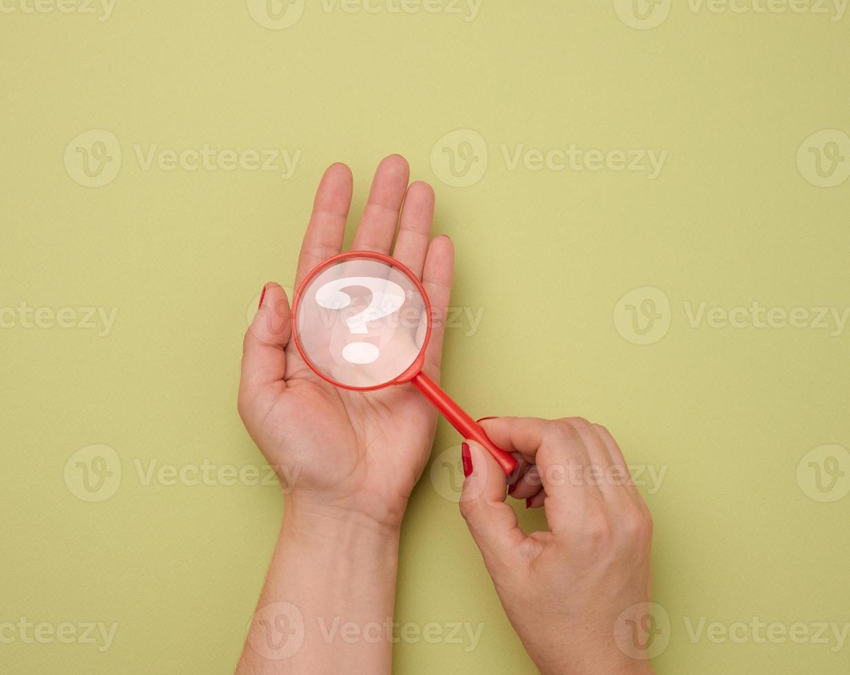 female hand holds a plastic magnifying glass and question marks on a green background. The concept of finding an answer to questions photo