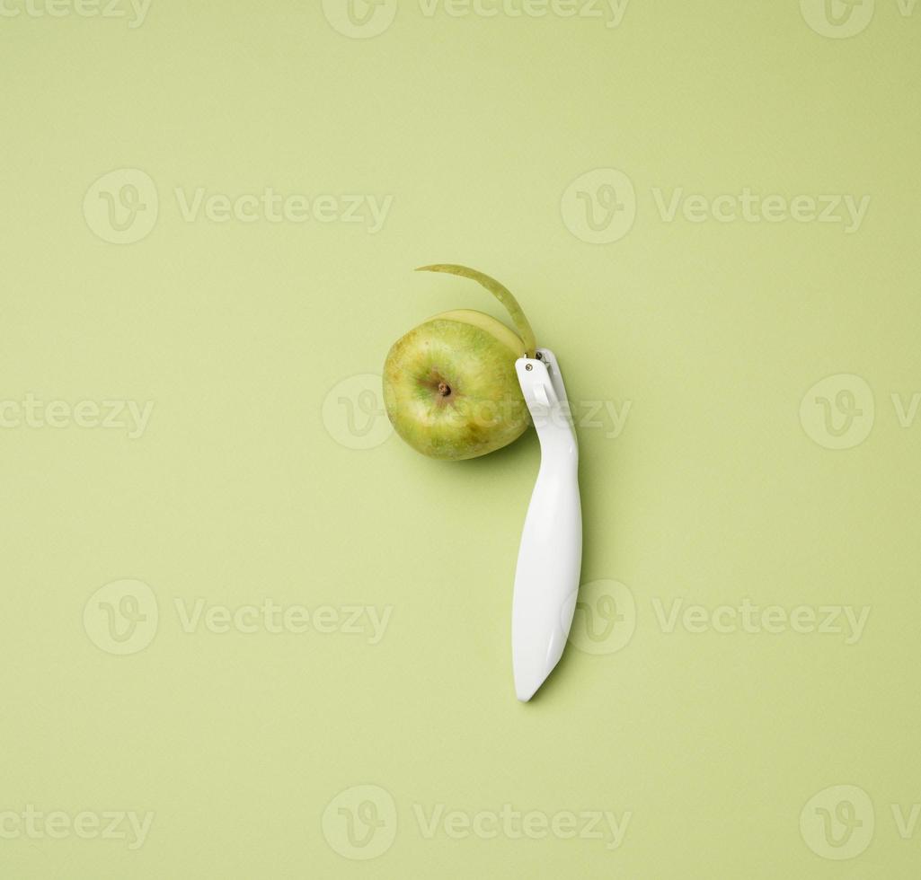 plastic knife for peeling vegetables, fruits and a green apple on a green background photo