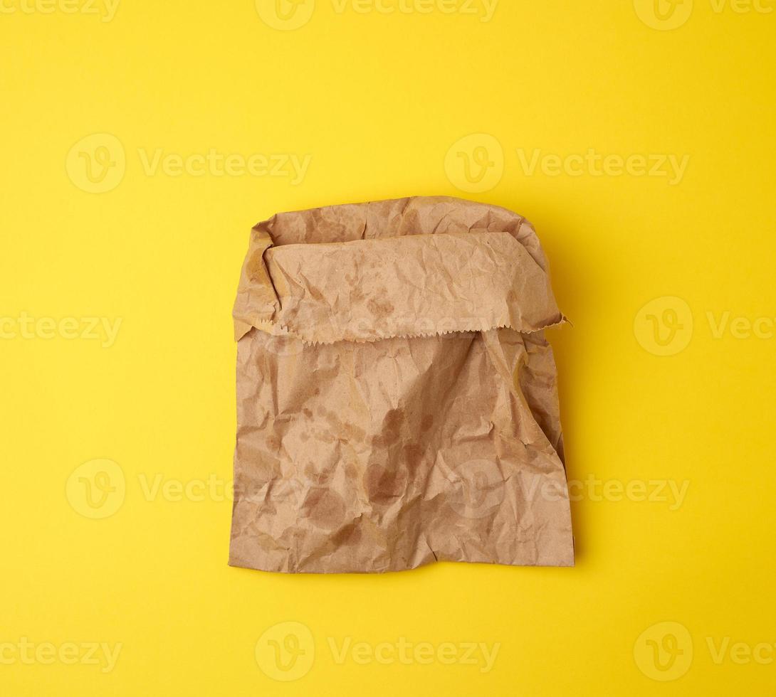 open brown paper bag for food packaging with greasy stains on a yellow background photo