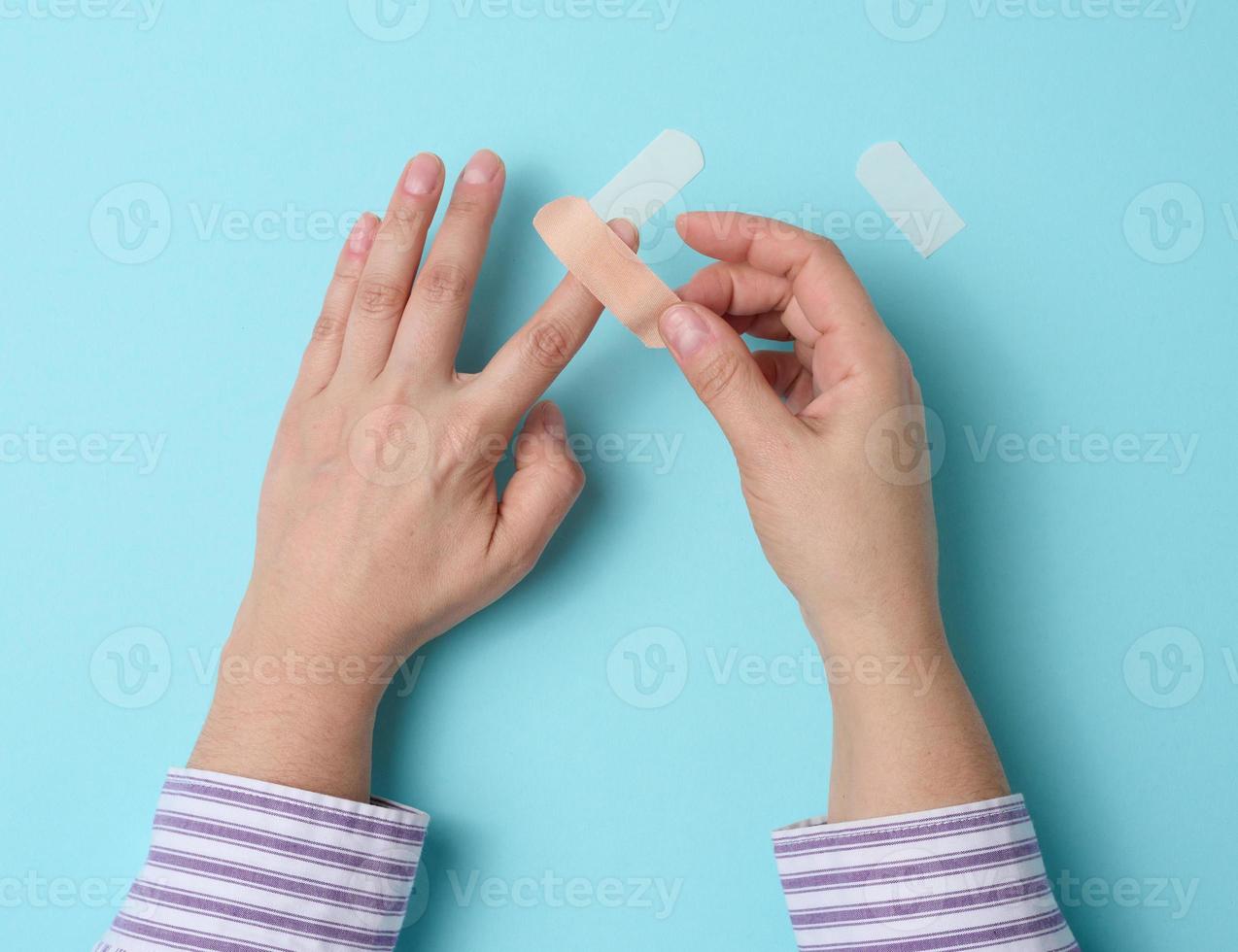 female hand and brown medical adhesive plaster for the treatment of injuries and cuts on the skin, blue background photo