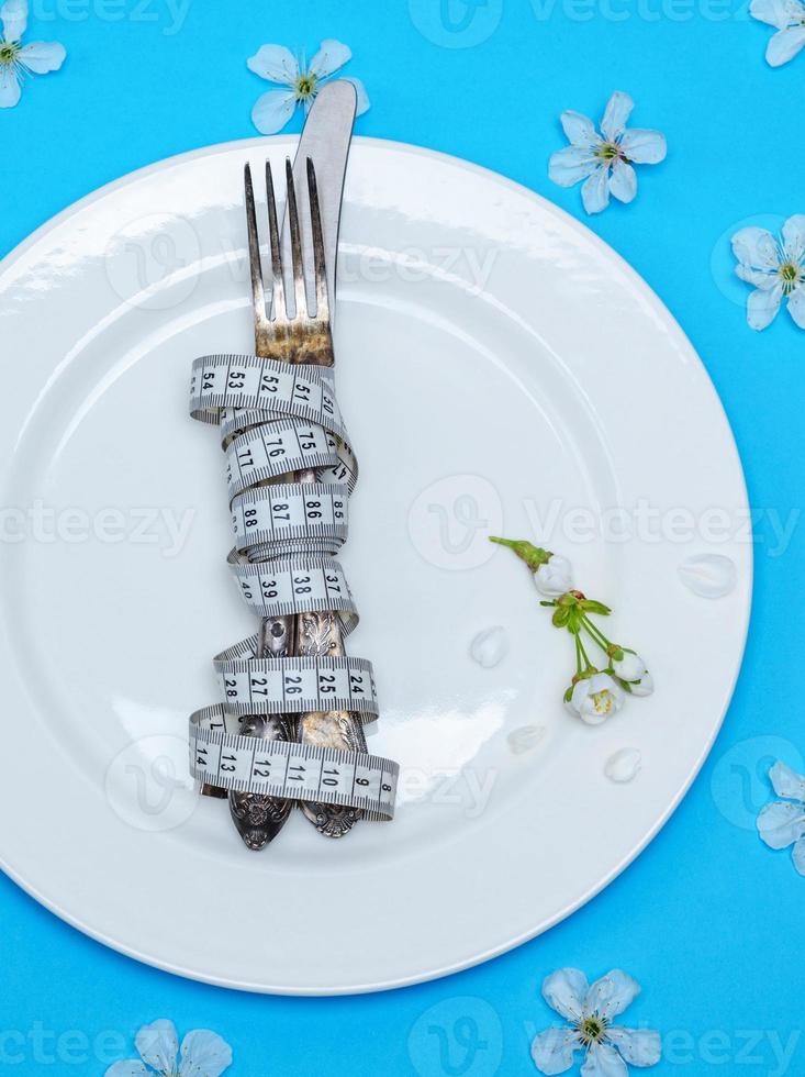 fork with a knife wrapped in a measuring tape lie on a white round ceramic plate photo