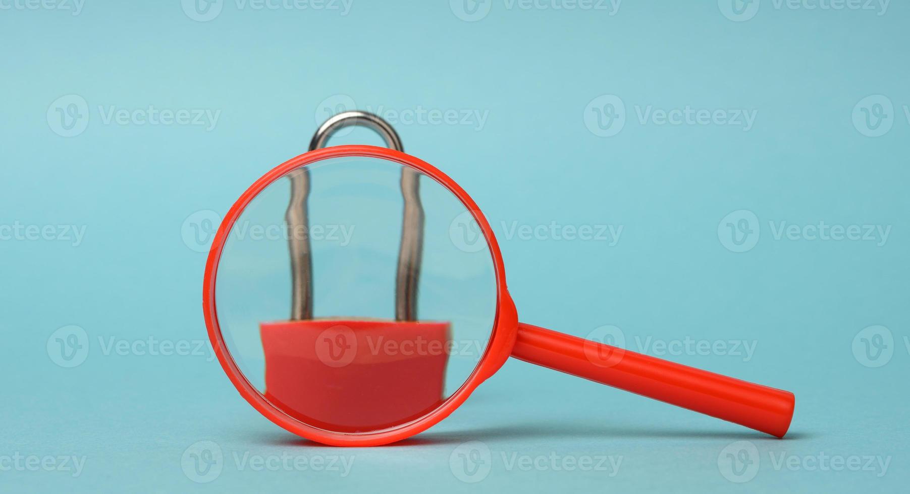 metal lock stands on a red plastic magnifying glass on a blue background. Data protection concept, personal information photo