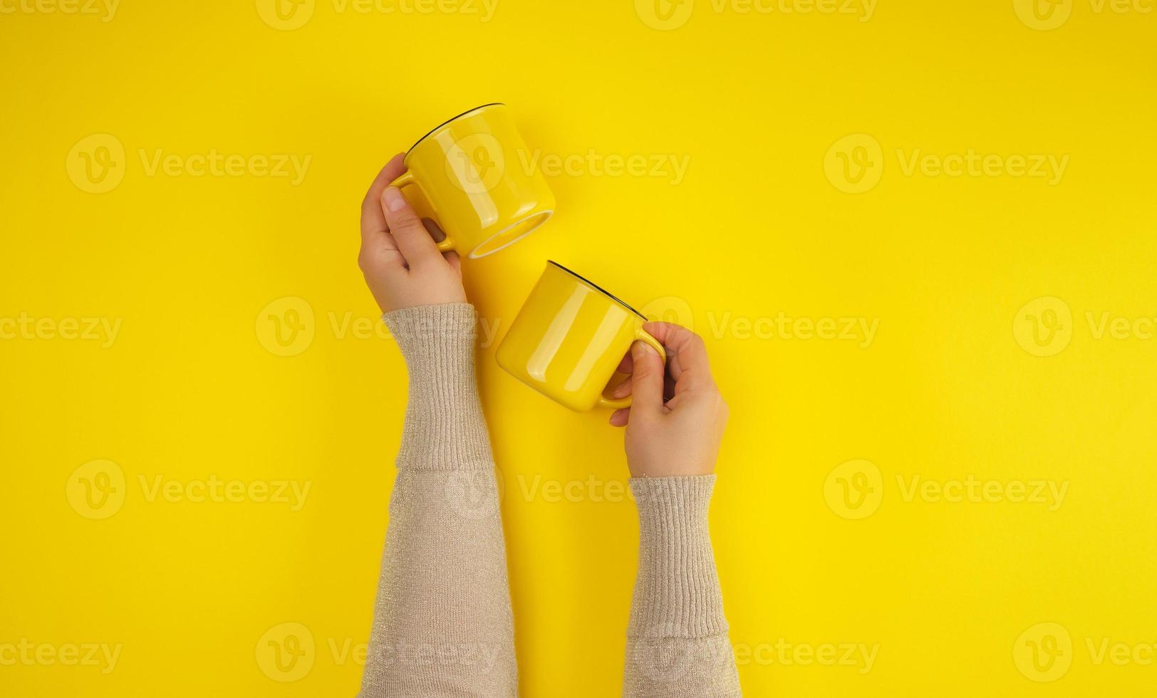 dos tazas de cerámica amarillas son apoyadas por una mano femenina sobre un fondo amarillo foto