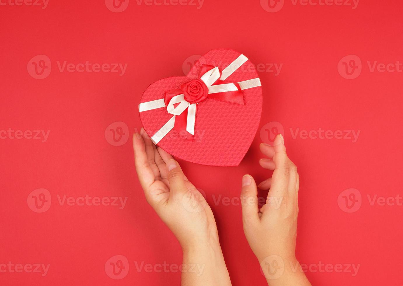 two hands hold a paper closed red box in the shape of a heart photo