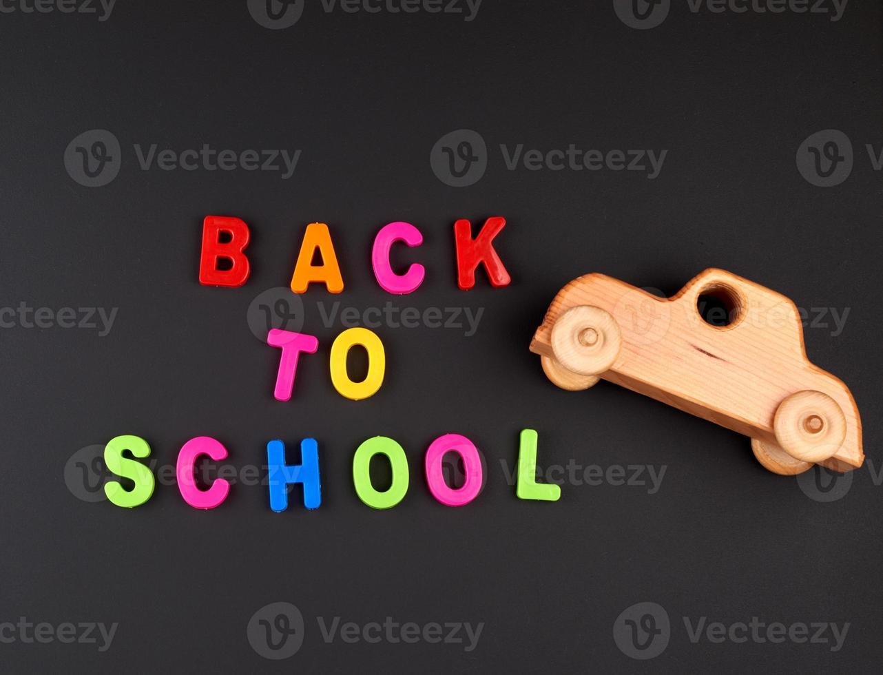 inscription back to school from multi-colored plastic letters and wooden baby car on black chalk board photo