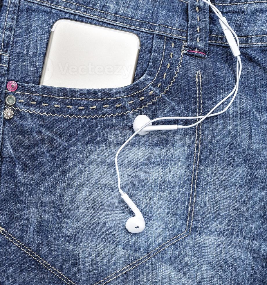 Smartphone in the front pocket of blue jeans and white headphones photo