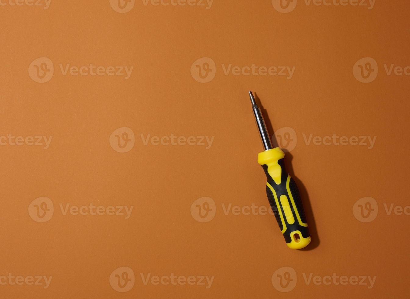 Screwdriver with a rubber handle on a brown background, close up photo