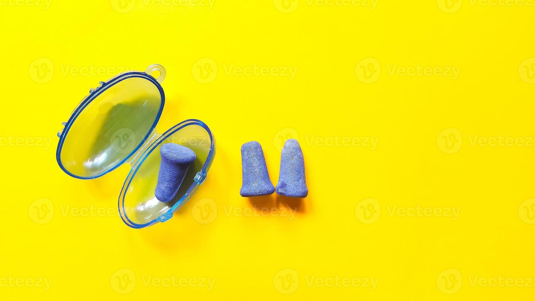 Soft blue foam earplugs in a plastic container and a pair of earplugs on yellow background photo