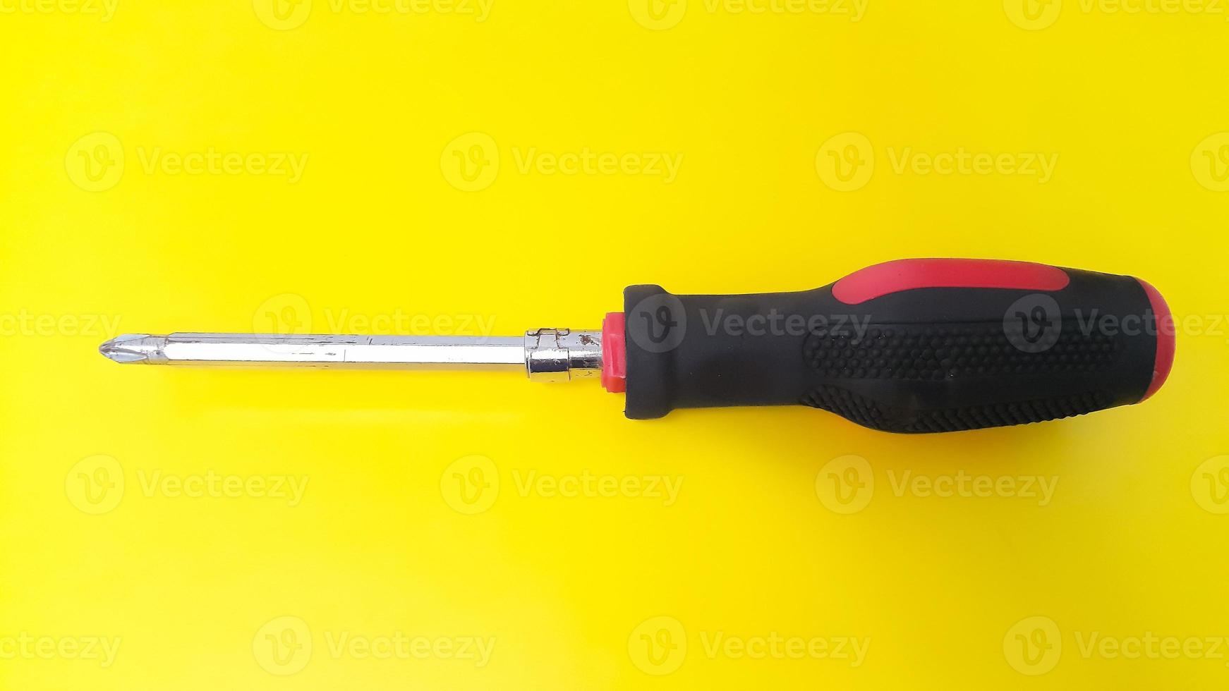 Close up of screwdriver with black and red handle isolated on yellow background photo