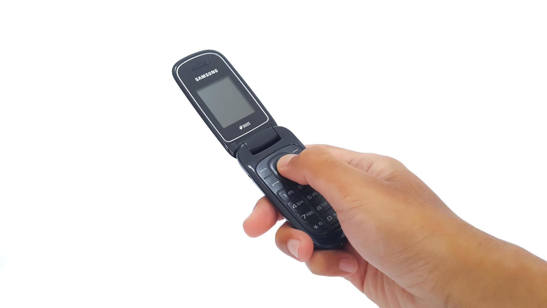 Jakarta, Indonesia, 2023 - Hand holding Samsung flip phone isolated on white background. Used obsolete open black Samsung flip cell phone. Obsolete open black Samsung flip cell phone. photo