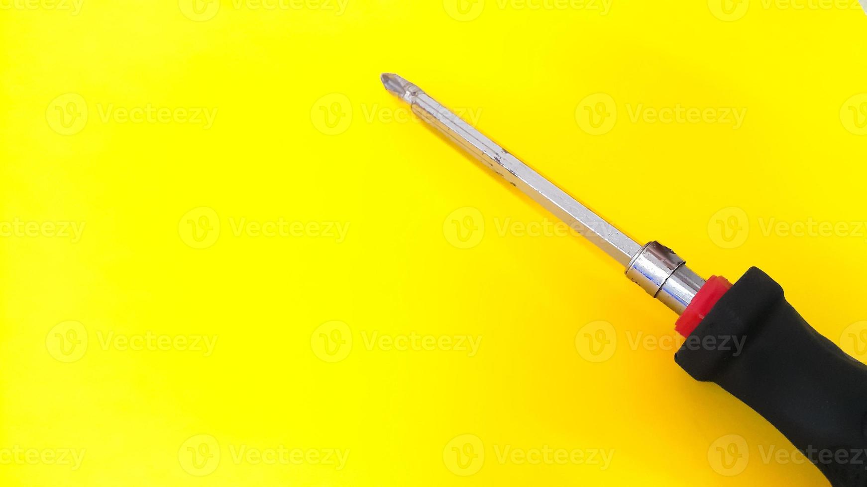 Close up of screwdriver with black and red handle isolated on yellow background photo