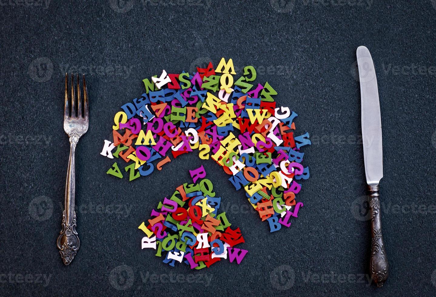 Cutlery and multicolored letters of wood on a black surface photo