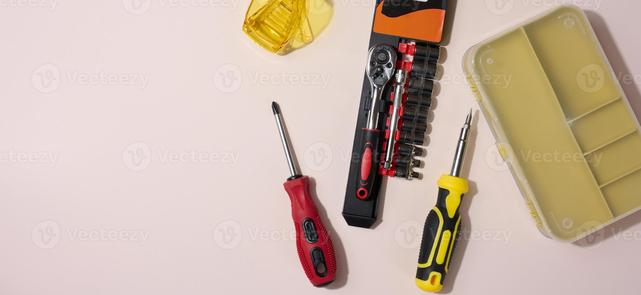 Transparent acrylic glasses and a screwdriver on a beige background, top view photo