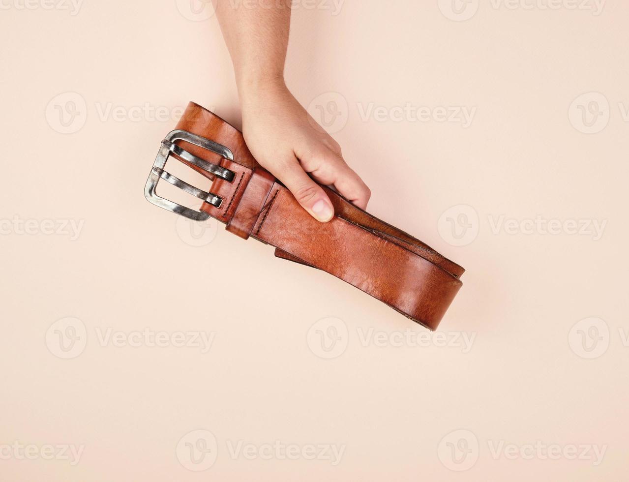 leather brown belt in a female hand on a beige background photo