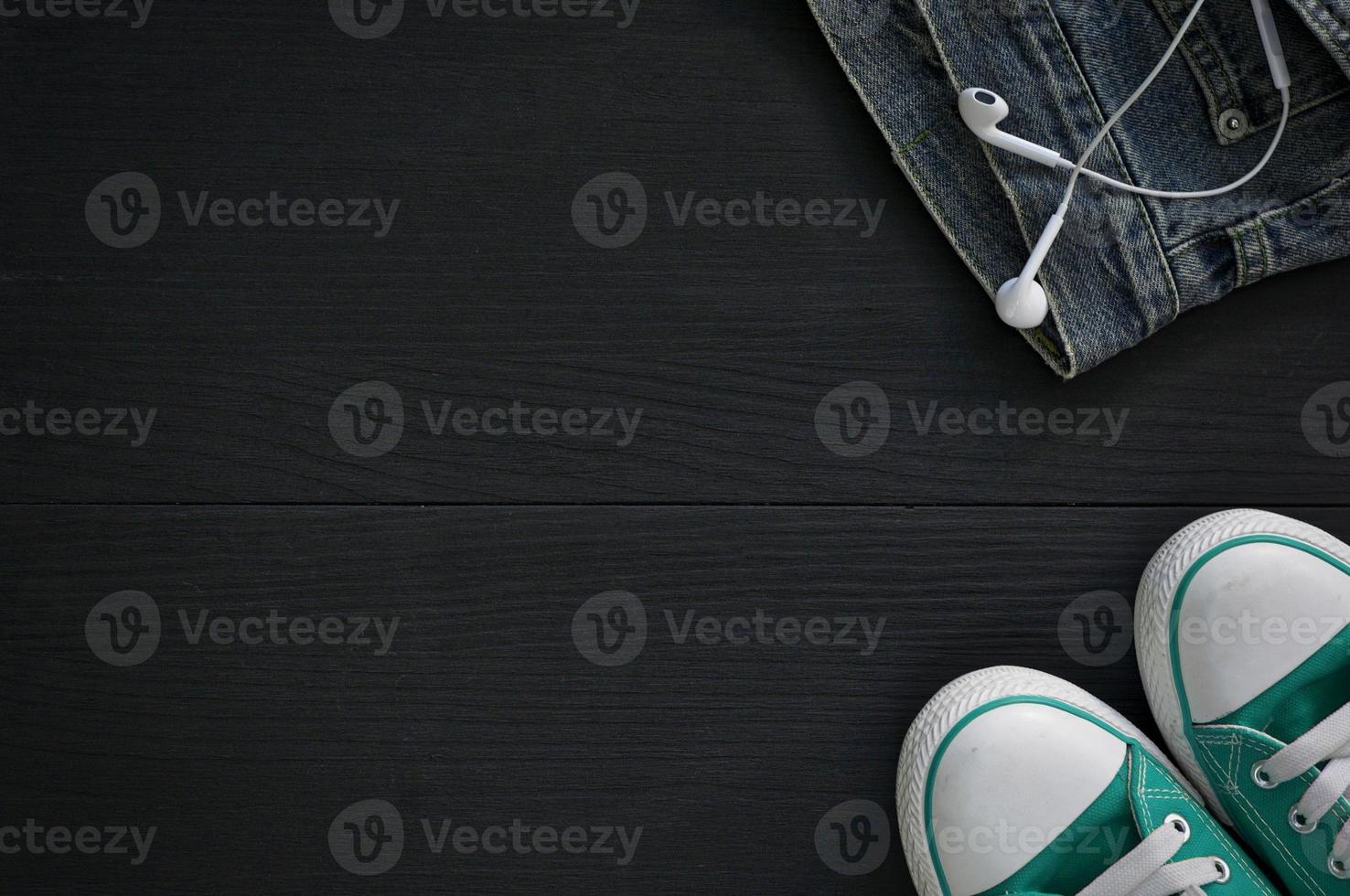 pair of sneakers, a fragment of jeans and headphones on a black wooden background photo