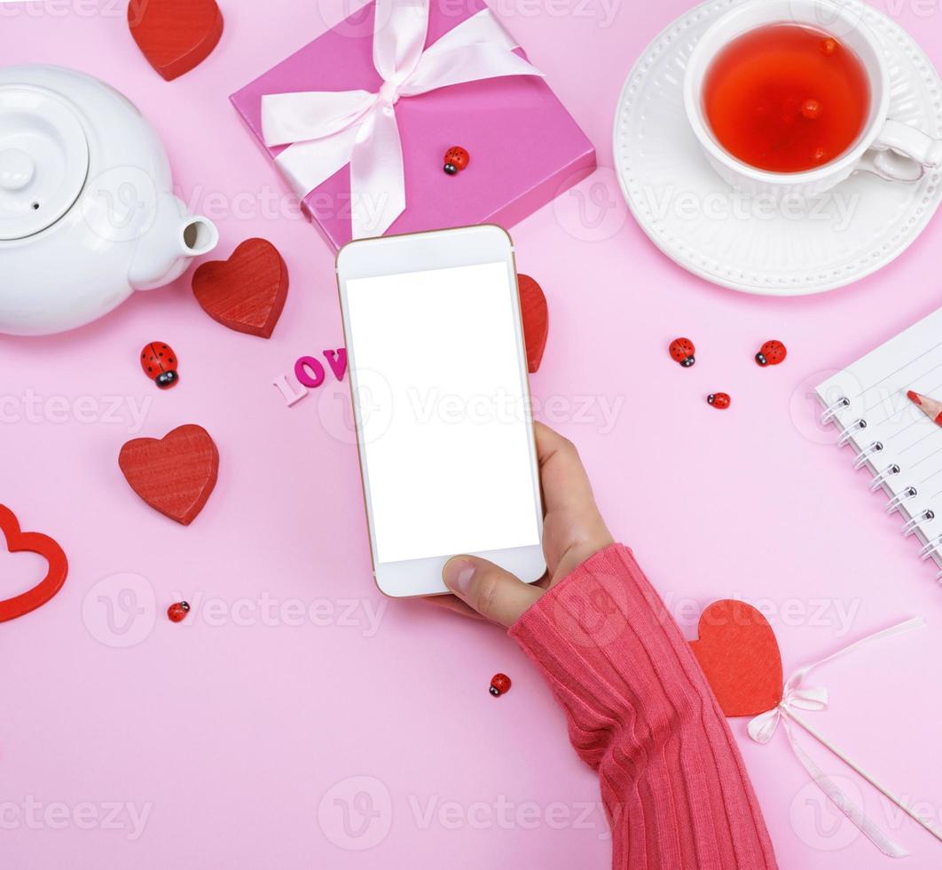 la mano derecha femenina en un suéter rosa sostiene un teléfono inteligente blanco foto