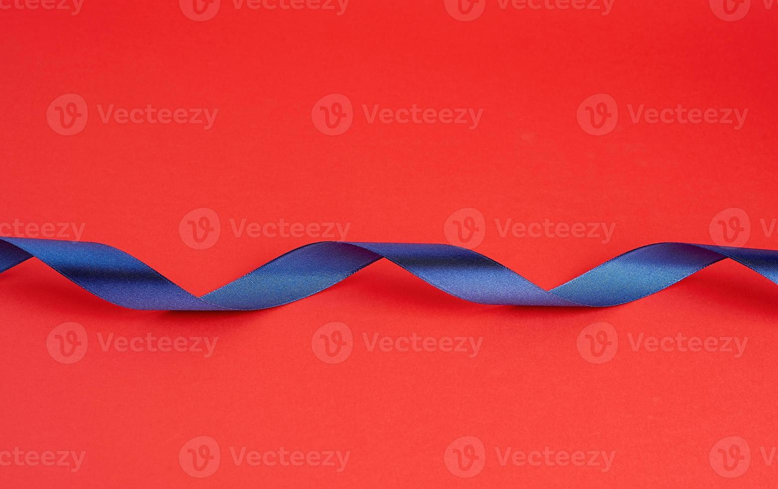 twisted dark blue silk shiny ribbon on a red background photo