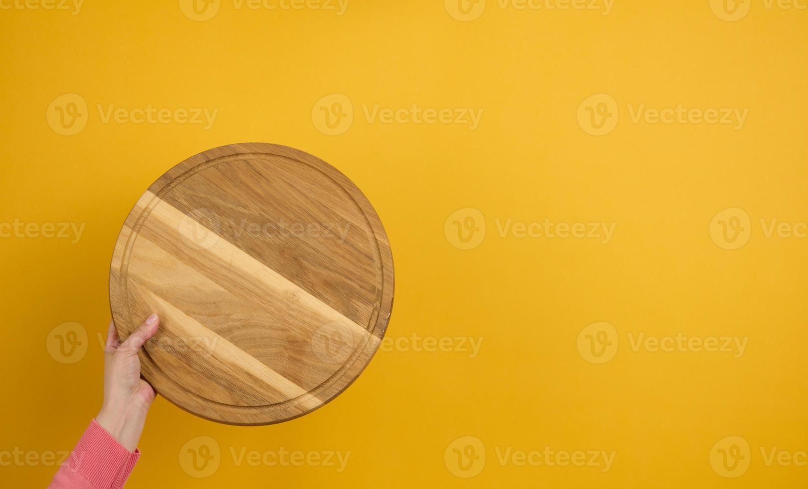 woman holding empty round wooden pizza board in hand, body part  on a yellow background photo