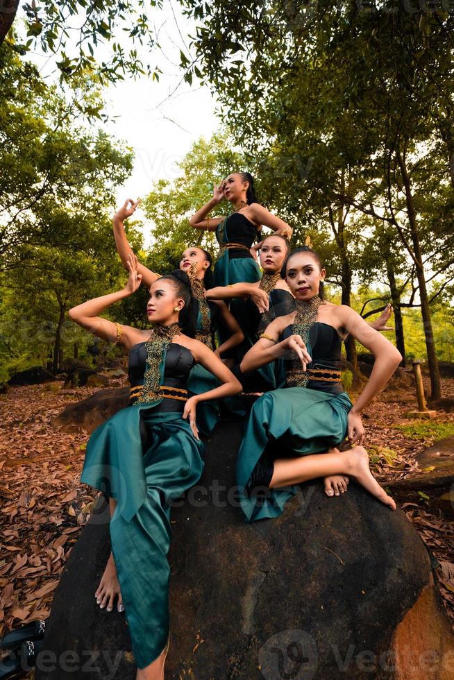 A Group of Asian people in green costumes sitting on a big rock with brown leaves in the background photo