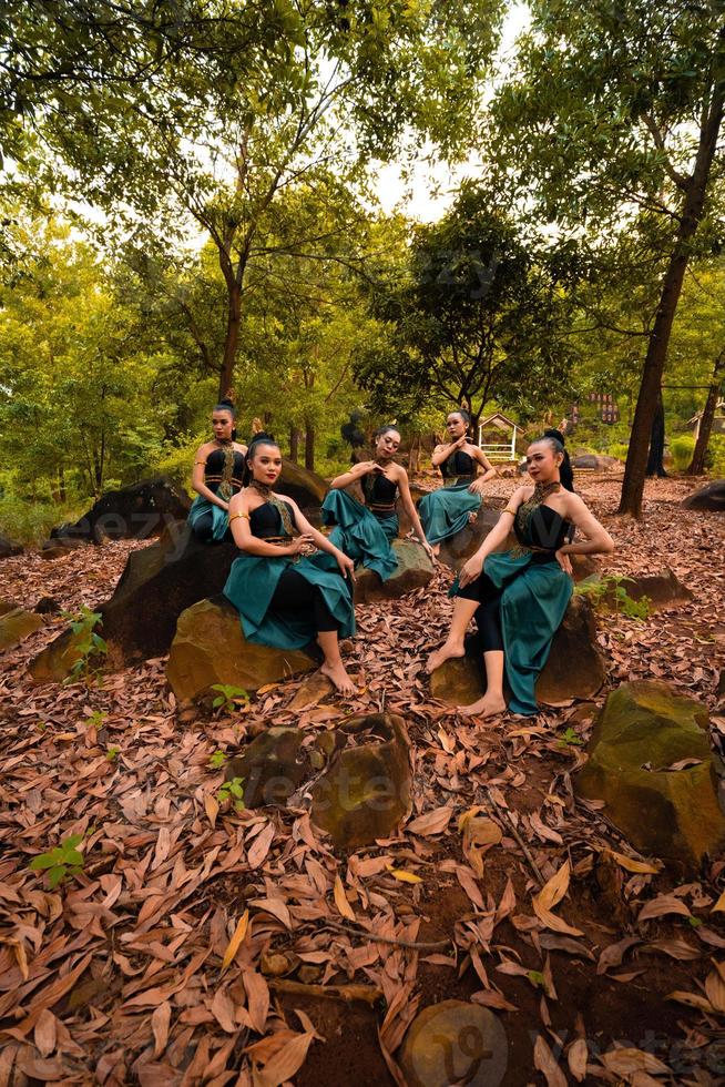 A Group of Asian women takes a vacation to the forest while wearing a green skirt and sitting on a rock photo