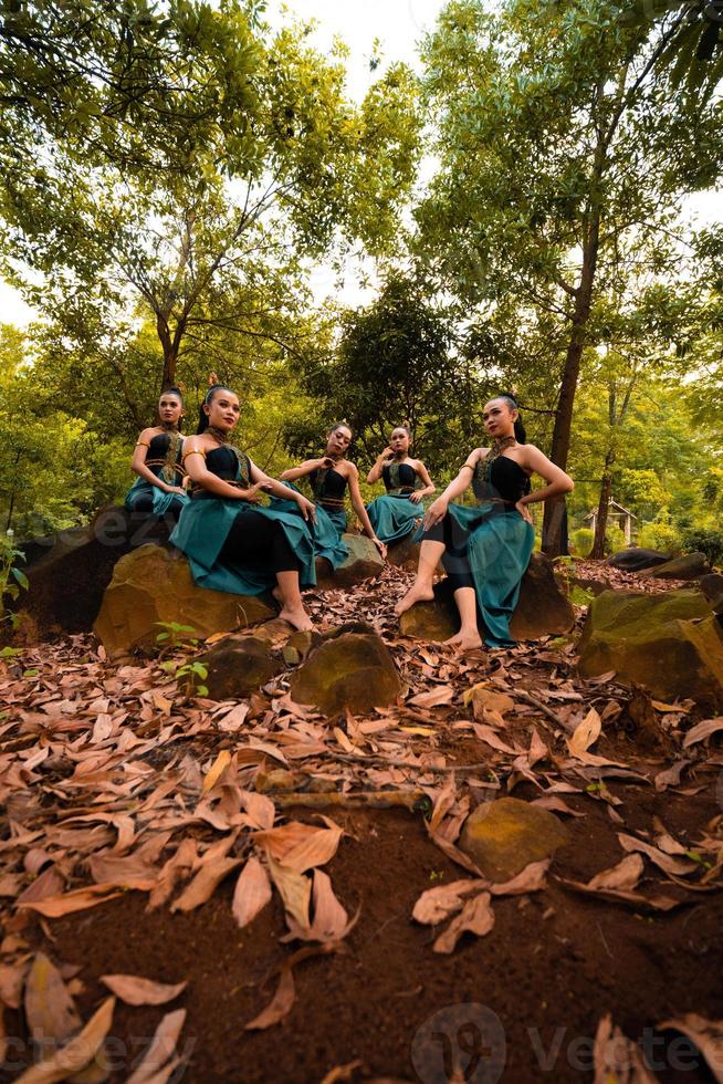 A Group of Asian women takes a vacation to the forest while wearing a green skirt and sitting on a rock photo