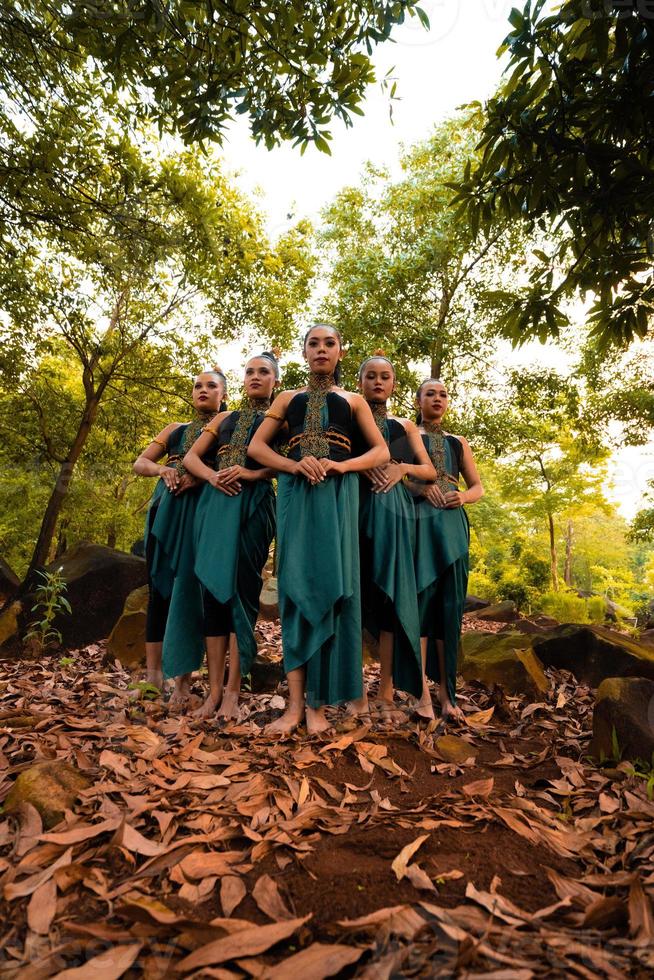 una toma amplia de una mujer asiática parada en el bosque mientras usa un traje de baile verde con hojas muertas foto