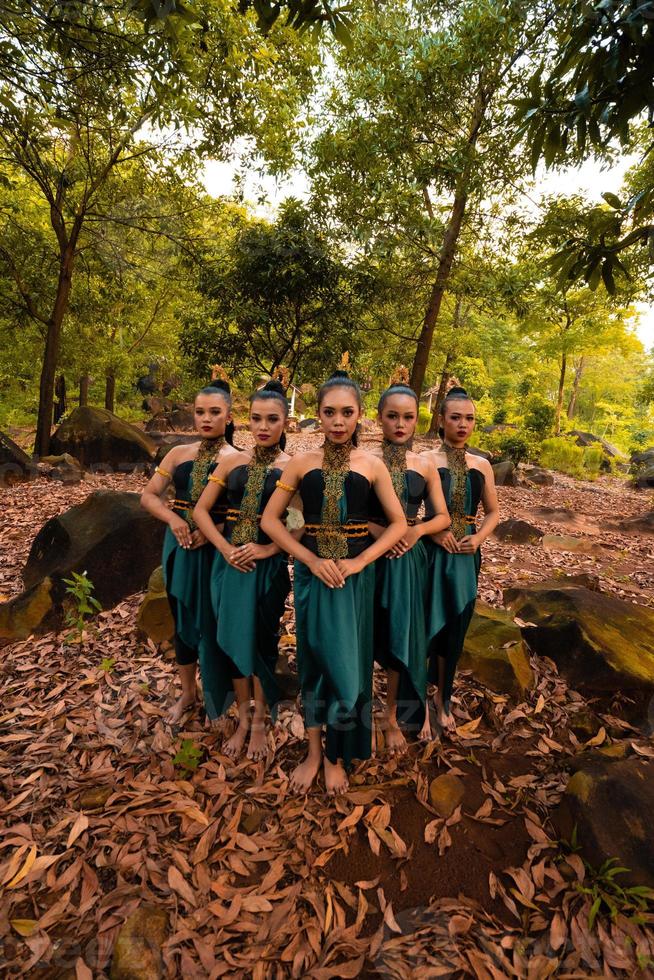 a wide shot of an Asian woman standing together in the forest while wearing a green dance costume with dead leaves photo