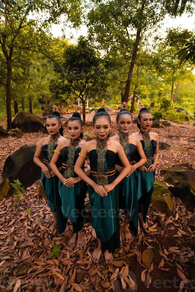 mujeres asiáticas glamorosas con disfraces verdes y maquillaje se alinean juntas en la jungla con hojas marrones en el suelo foto